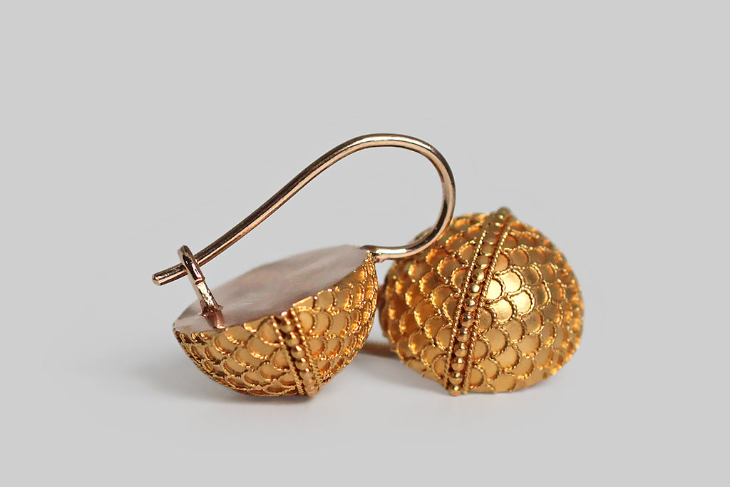 A charming pair of Victorian-era drop earrings, modeled as half orbs, in 14k yellow gold. These curved faces of these orbs are covered with a delicate pattern of scallops or scales, made with applied, Etruscan-style wirework. A row of tiny granulated beads acts as an equator, dividing the orbs into hemispheres. This decor is exceptionally fine, and the perfect repetition in the design is especially winning. 