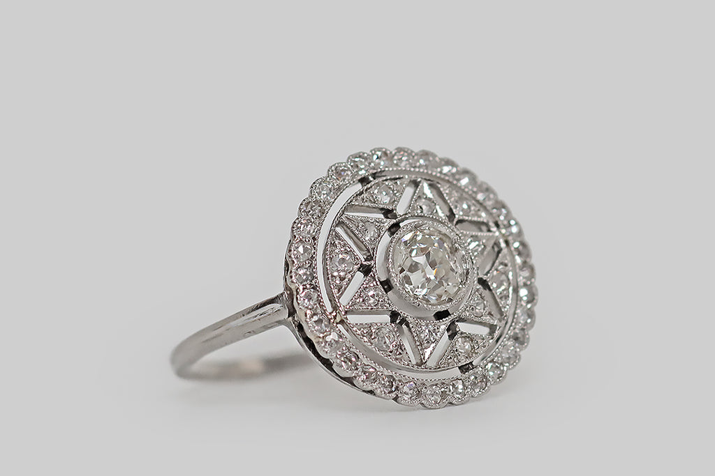 Antique Jewelry Portland, Vintage Jewelry Portland , Antique Engagement Rings | Poor Mouchette | An early 20th century engagement ring, modeled in platinum, whose central gem is a lively, .40 carat old mine cut diamond. This vibrant, white, hand-cut diamond floats in a round, milgrained bezel at the center of the ring’s six-pointed star motif. This star shape is created by a series of diamond-set, pennant-shaped seats that surround the larger, central diamond.