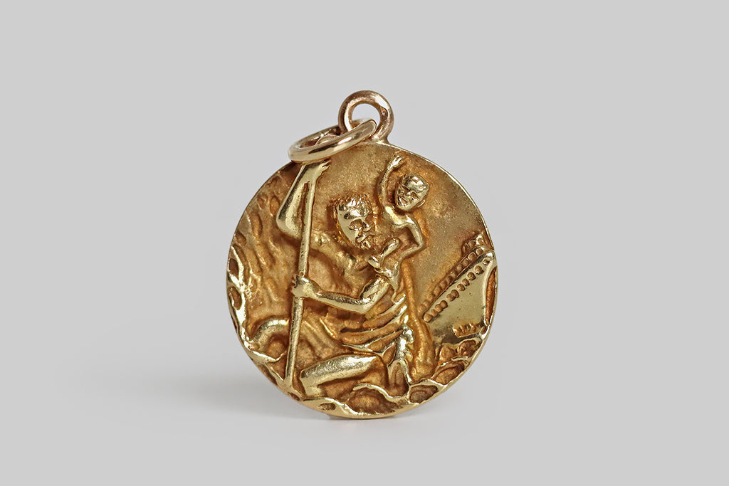 Poor Mouchette | Curated Antique Jewelry, Vintage Jewelry & Engagement Rings | Portland, Oregon | A very cool, mid-20th-century, Saint Christopher medal, modeled in 14k yellow gold, that features a richly-textured, high-relief carving of the beloved saint. In this miniature scene, Saint Christopher is depicted standing amid waves— behind him, in the distance, an ocean liner approaches. The ever-present rescued child sits atop Christopher's left shoulder, looking especially happy. 