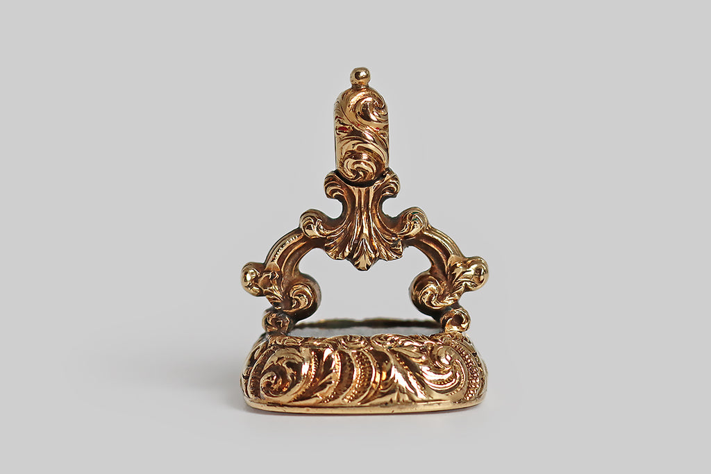 Poor Mouchette | Curated Antique Jewelry, Vintage Jewelry & Engagement Rings | Portland, Oregon | A wonderful, large fob (late-Georgian/early-Victorian fob), modeled in 14k yellow gold and set with a rectangular, intaglio-carved, bloodstone gem. This finely-carved wax seal features a coat of arms, atop which sits a coronet-collared dragon. This coat of arms is "impaled" to indicate a marriage— on the sinister side, we have a series of three seashells and a small star