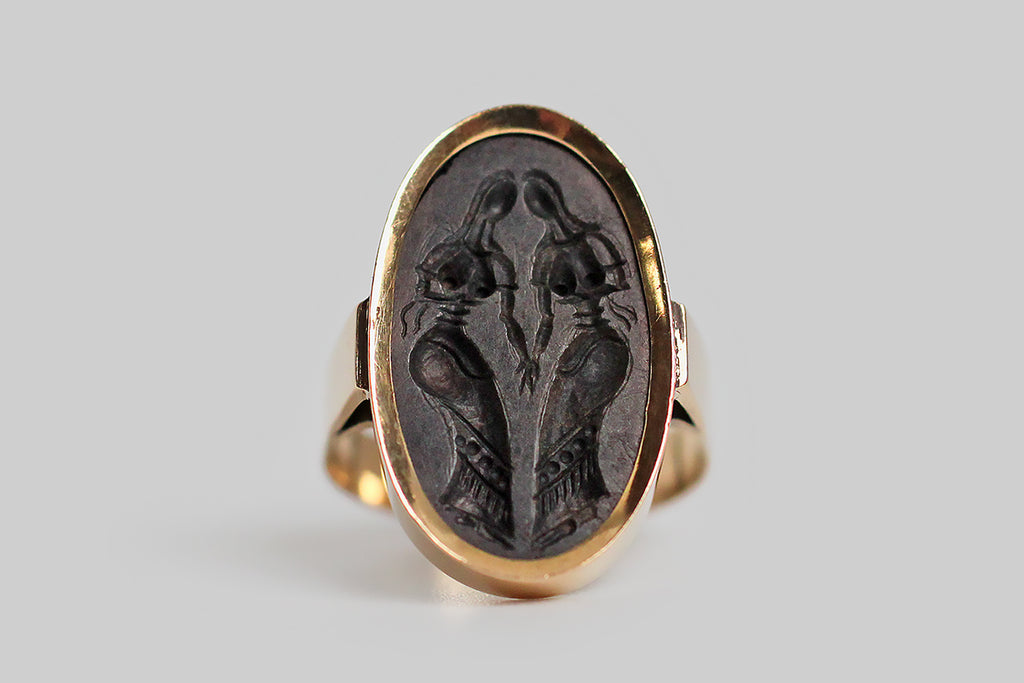 Poor Mouchette | Curated Antique Jewelry, Vintage Jewelry & Engagement Rings | Portland, Oregon | A striking antique ring, modeled in rosy 18k yellow gold, whose gem is an unusual, intaglio-carved, gutta percha cabochon. This mysterious old intaglio is held in a smooth, weighty, recessed bezel— it depicts two women, with graceful, curvaceous figures. These twin-like women face one another, holding hands, their foreheads almost touching; they appear to be corseted, and they wear embellished garments. 