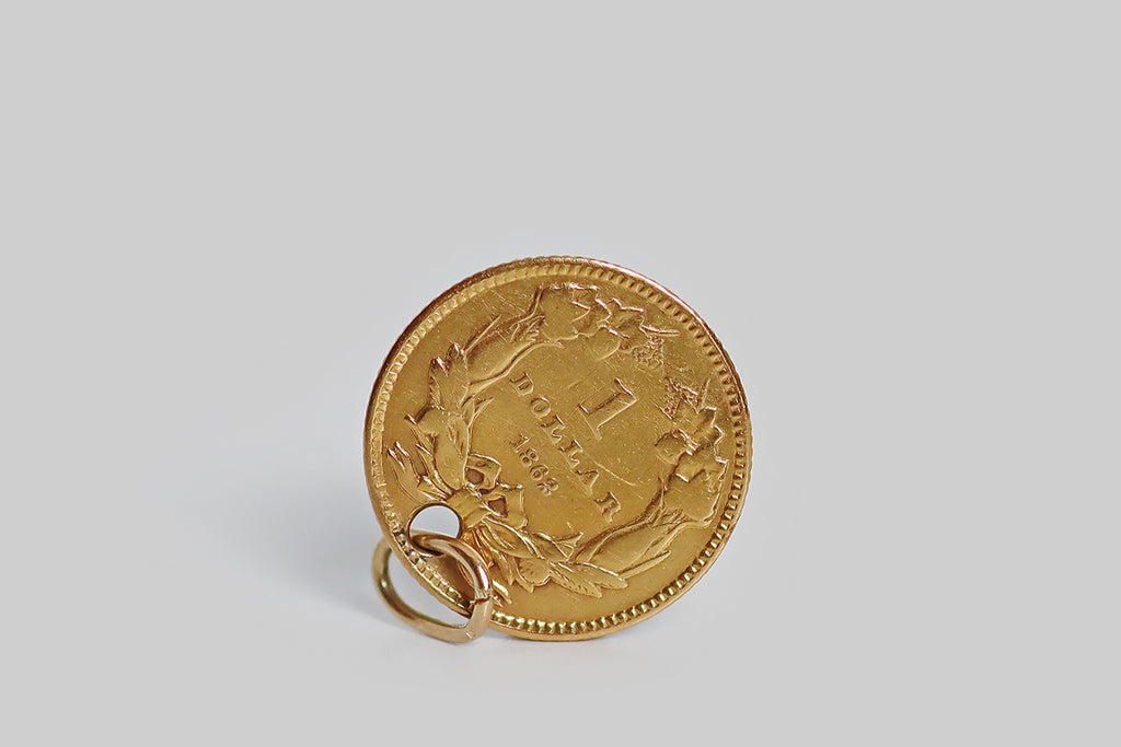 An original 1852 (civil war era) type-3 Liberty Dollar (90% gold, or approx 22k) designed by the American portraitist and engraver James B Longacre, holed and fitted with a 14k gold jump ring so it can be worn as a pendant or charm. This little coin features a left facing bust of liberty