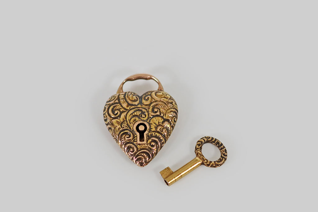 Antique Jewelry Portland, Vintage Jewelry Portland , Antique Engagement Rings | Poor Mouchette | A lovely Victorian-era, repoussé heart padlock, modeled in 14k yellow gold, that is still partnered with its original 14k gold key! This antique charm is a functioning lock, and it is in wonderful condition. The heart-shaped lock is decorated all-over with flowers and fine, swirling, baroque forms, and the key's top echos this motif.