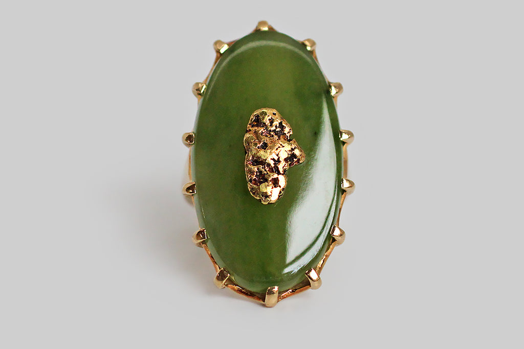 A dramatic vintage ring, modeled in 10k yellow gold, featuring a large, oval, nephrite jade cabochon, upon which a shapely, natural gold nugget is mounted. Our luminous slab of moss-green jade is held in the ring’s crown-like, fourteen-prong head. The nugget is riveted to the jade, so that it appears to float in a green field. The ring's gallery is scalloped and carved to accentuate the prongs.