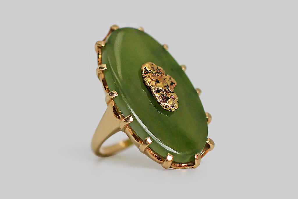 A dramatic vintage ring, modeled in 10k yellow gold, featuring a large, oval, nephrite jade cabochon, upon which a shapely, natural gold nugget is mounted. Our luminous slab of moss-green jade is held in the ring’s crown-like, fourteen-prong head. The nugget is riveted to the jade, so that it appears to float in a green field. The ring's gallery is scalloped and carved to accentuate the prongs.