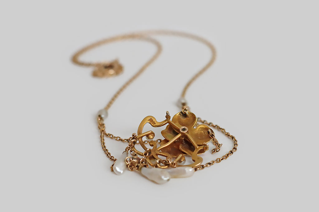 Poor Mouchette | Curated Antique Jewelry, Vintage Jewelry & Engagement Rings | Portland, Oregon | A beautiful, Art Nouveau era festoon necklace, modeled in rosy 14k yellow gold, whose focal point is a cheerful pansy blossom, decorated with iridescent, multi-color enamel. This sweet, pastel pansy rests inside a shapely Art Nouveau frame. White seed pearls decorate the frame, while a trio of natural river pearls dangle below it; further small pearls decorate the necklace’s chain