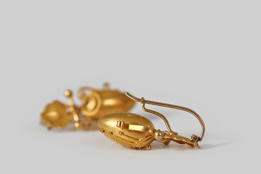 Antique Jewelry Portland, Vintage Jewelry Portland , Antique Engagement Rings | Poor Mouchette | A pair of antique, Victorian-era earrings, made in the Etruscan style, and modeled in 14k yellow gold. These elegant earrings were designed with shell-form tops, below which hang drops made to resemble Greek amphorae. A barbell joins these two elements, allowing the amphorae to swing, gently, with movement. The earwires are locking kidney wires, and they are hinged at the top.
