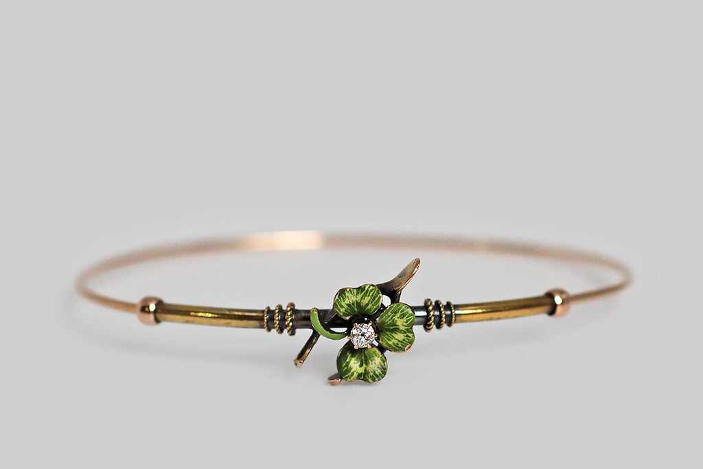 A slender, Victorian-era bangle bracelet, modeled in 14k gold, whose face is adorned with two good luck charms— a wishbone and a beautifully hand painted, polychrome enamel clover. A .10 carat old mine cut diamond rests, in claw-like prongs, at the center of this lucky composition. Trios of graduated rope details encircle the gold tube that comprises the bracelet face, where they flank the bracelet's figural centerpiece.