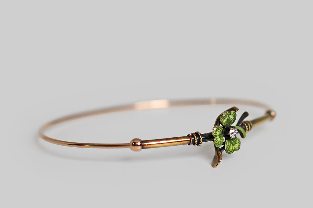 A slender, Victorian-era bangle bracelet, modeled in 14k gold, whose face is adorned with two good luck charms— a wishbone and a beautifully hand painted, polychrome enamel clover. A .10 carat old mine cut diamond rests, in claw-like prongs, at the center of this lucky composition. Trios of graduated rope details encircle the gold tube that comprises the bracelet face, where they flank the bracelet's figural centerpiece. 