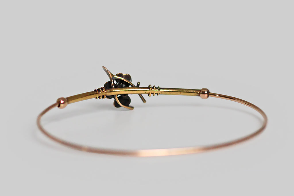 A slender, Victorian-era bangle bracelet, modeled in 14k gold, whose face is adorned with two good luck charms— a wishbone and a beautifully hand painted, polychrome enamel clover. A .10 carat old mine cut diamond rests, in claw-like prongs, at the center of this lucky composition. Trios of graduated rope details encircle the gold tube that comprises the bracelet face, where they flank the bracelet's figural centerpiece. 