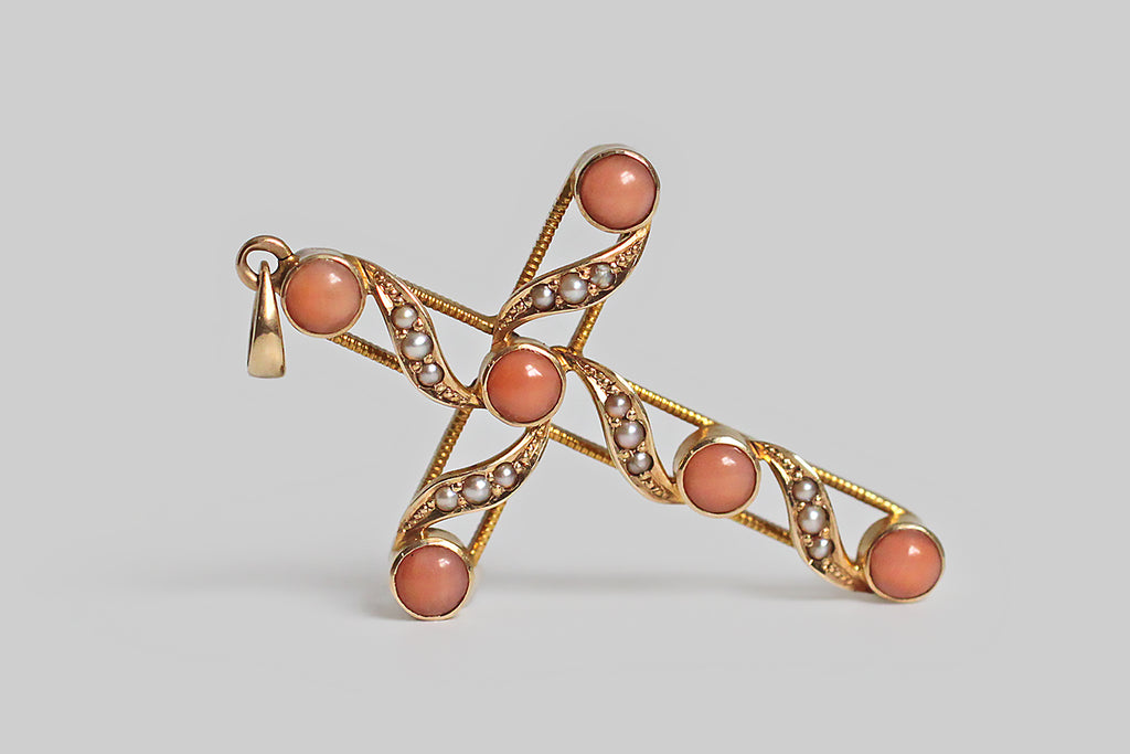 A late-Victorian, cross-shaped pendant, made in 14k yellow gold, embellished with natural coral cabochons and a bevy natural, silvery, seed pearls. This cross is beautifully made, with an airy, open-work character. Its six, pinkish-orange corals are set in smooth bezels— ribbon like forms weave between the coral stations, and each of these is bead-set with three seed pearls. The graceful movement of these ribboning forms calls to mind the image of a cloth draped cross, 