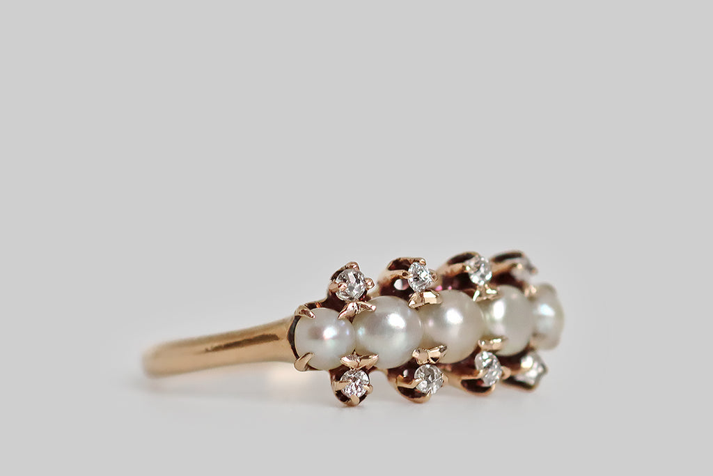 Poor Mouchette | Curated Antique Jewelry, Vintage Jewelry & Engagement Rings | Portland, Oregon | A delicate, Victorian-era cluster ring, modeled in 14k rosy-yellow gold, whose five primary gems are a series of luminous, white half-pearls. These pearls are set horizontally, across the curved ring face, in shared claw-like prongs. They are subtly graduated, with the largest pearl resting at center. Eight, small, old mine cut diamonds further decorate the ring face