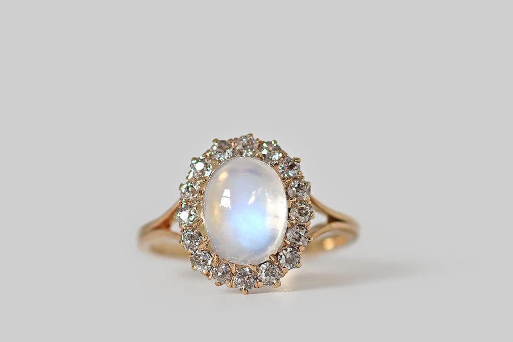 Poor Mouchette | Curated Antique Jewelry, Vintage Jewelry & Engagement Rings | Portland, Oregon | An Edwardian era ring, modeled in 14k rosy yellow gold, whose primary gem is a soulful, blue flash moonstone cabochon. This high-dome, oval moonstone is transparent, with a strong, shimmery blue flash that shifts with movement. It is held in sixteen tapering, claw-like prongs, and surrounded by a glittering halo of sixteen old mine cut diamonds. 