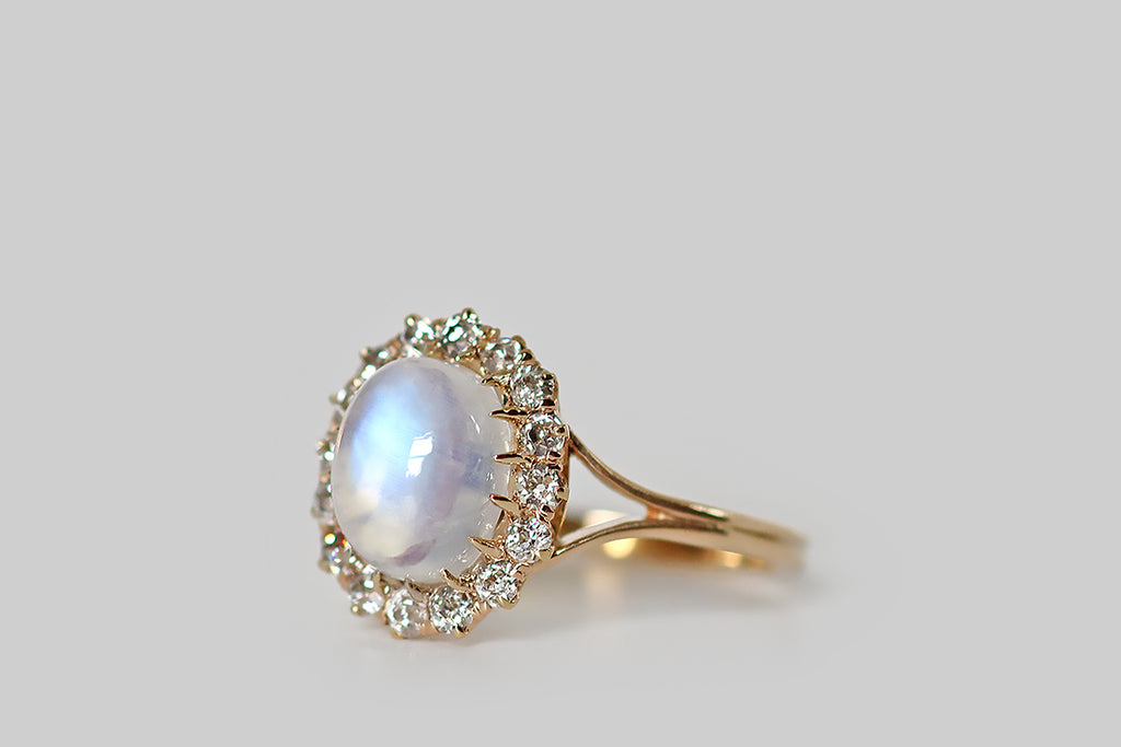 Poor Mouchette | Curated Antique Jewelry, Vintage Jewelry & Engagement Rings | Portland, Oregon | An Edwardian era ring, modeled in 14k rosy yellow gold, whose primary gem is a soulful, blue flash moonstone cabochon. This high-dome, oval moonstone is transparent, with a strong, shimmery blue flash that shifts with movement. It is held in sixteen tapering, claw-like prongs, and surrounded by a glittering halo of sixteen old mine cut diamonds.