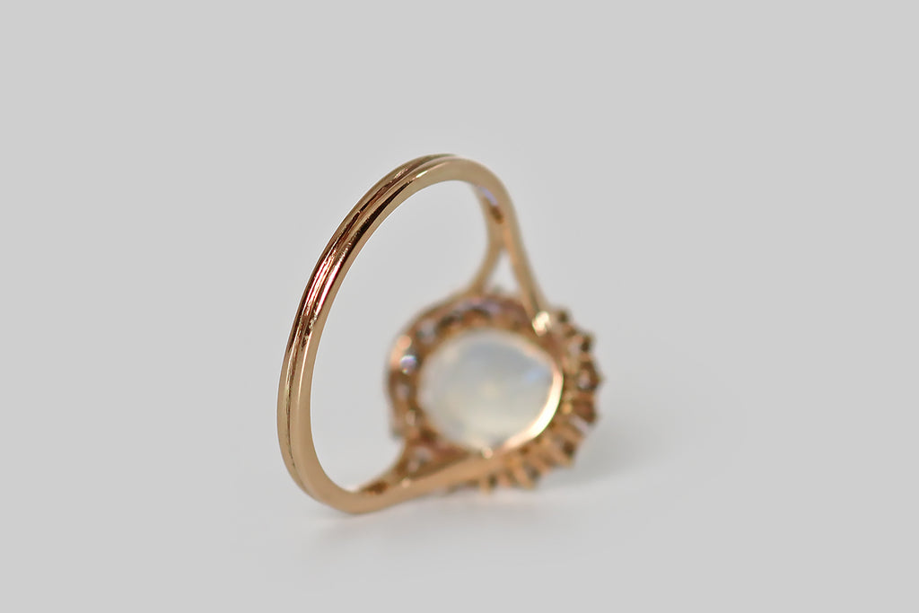 Poor Mouchette | Curated Antique Jewelry, Vintage Jewelry & Engagement Rings | Portland, Oregon | An Edwardian era ring, modeled in 14k rosy yellow gold, whose primary gem is a soulful, blue flash moonstone cabochon. This high-dome, oval moonstone is transparent, with a strong, shimmery blue flash that shifts with movement. It is held in sixteen tapering, claw-like prongs, and surrounded by a glittering halo of sixteen old mine cut diamonds.