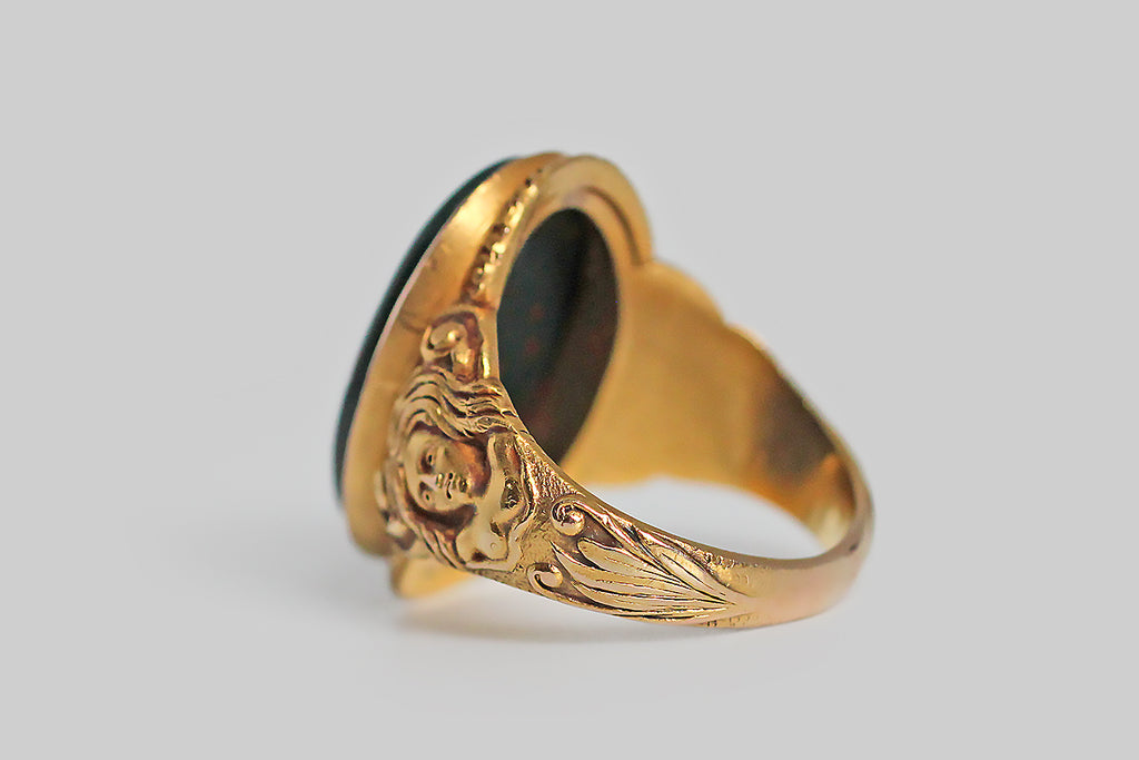 A strange and wonderful Victorian-era ring, modeled in bloomed 14k yellow gold, whose shoulders are occupied by a pair of dryads. These finely-carved maidens have long, flowing hair . . . their bare chests transition into a tree-like body, below which sprigs of plant life grow. The curling figures that decorate the ring's shoulders suggest the dryads' up-stretched arms, transforming into limbs. We think this unusual decor probably references the myth of Daphne