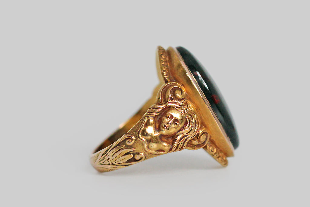 A strange and wonderful Victorian-era ring, modeled in bloomed 14k yellow gold, whose shoulders are occupied by a pair of dryads. These finely-carved maidens have long, flowing hair . . . their bare chests transition into a tree-like body, below which sprigs of plant life grow. The curling figures that decorate the ring's shoulders suggest the dryads' up-stretched arms, transforming into limbs. We think this unusual decor probably references the myth of Daphne