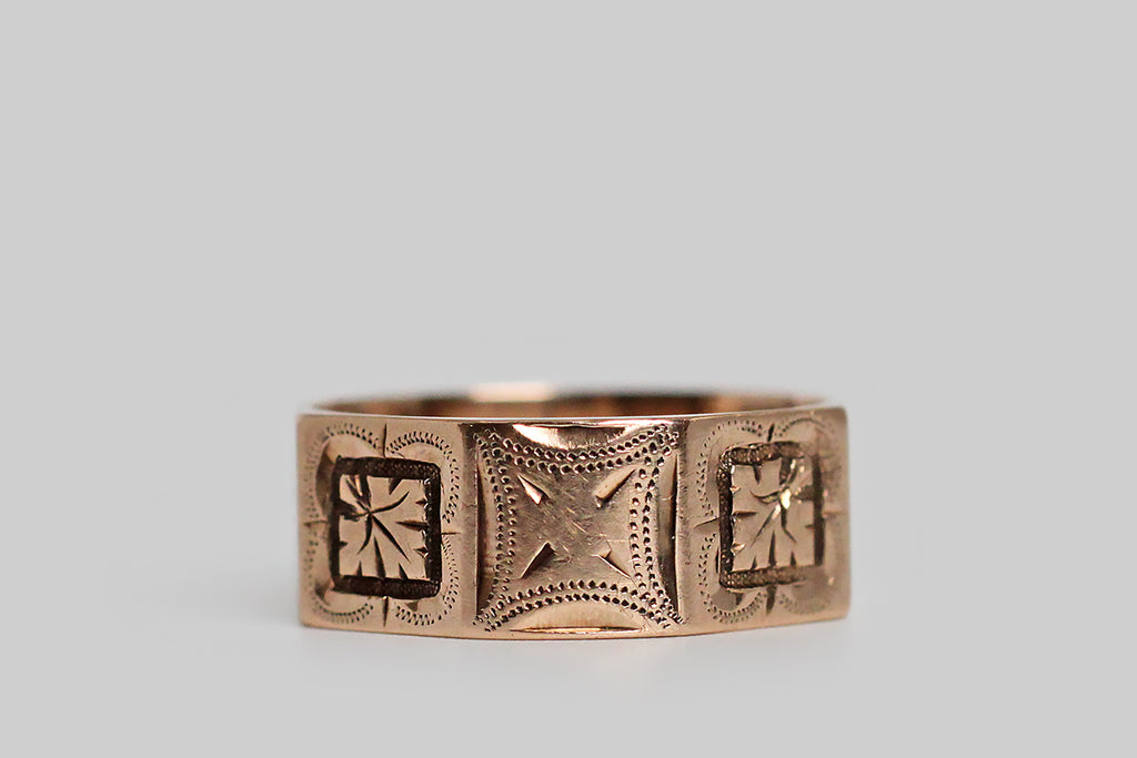 An antique, Victorian era, cigar band wedding ring, modeled in 14k rose gold. This wide band ring has a charming octagonal surface, composed of square panels, and each of these panels is decorated with beautiful, hand-engraved decor. This decor is an alternating pattern of deeply-carved oak leaves and orange blossoms, each resting atop a more subtle, four-lobed, clover-shaped engraving. Orange blossoms have long symbolized fertility and purity, while oak leaves stand for strength, faith