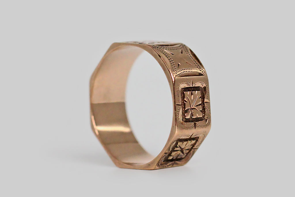 An antique, Victorian era, cigar band wedding ring, modeled in 14k rose gold. This wide band ring has a charming octagonal surface, composed of square panels, and each of these panels is decorated with beautiful, hand-engraved decor. This decor is an alternating pattern of deeply-carved oak leaves and orange blossoms, each resting atop a more subtle, four-lobed, clover-shaped engraving. Orange blossoms have long symbolized fertility and purity, while oak leaves stand for strength, faith