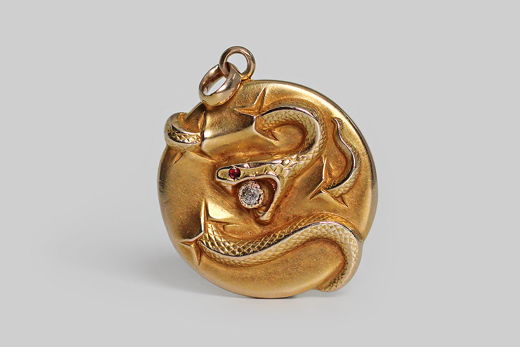 Poor Mouchette | Curated Antique Jewelry, Vintage Jewelry & Engagement Rings | Portland, Oregon | A late Victorian, figural, repoussé, locket, modeled in 10k yellow gold, whose subject is a snake, its curving body seeming to break through the locket’s surface, here and there, as if it were a drum’s head, or a taut sheet of paper. Our snake closes its jaws around a small, bezel set, old mine cut diamond. Its eye is set with a vibrant, red, cabochon ruby. 