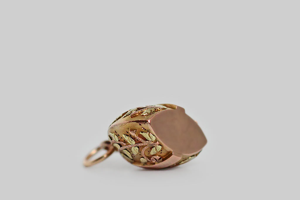 A sweet, miniature, Victorian era fob, modeled in yellow, rose, and green 10k gold. This weight-shaped charm is decorated with masterfully hand-sawed leaves and flowers. The tiny plant forms were applied, piece by piece, to the surface of the charm— they bend gracefully, and have a somewhat fantastical appearance, with their circular, nodding blooms and arrow-shaped seed heads. 
